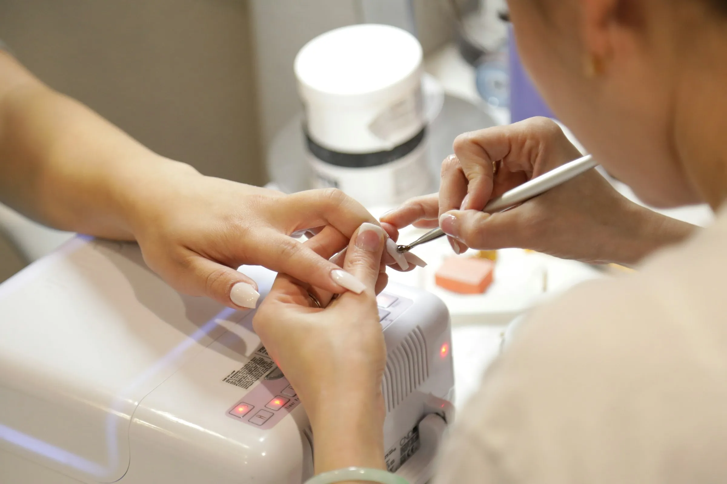 A manicurist shaping a client's nails at a lit work table