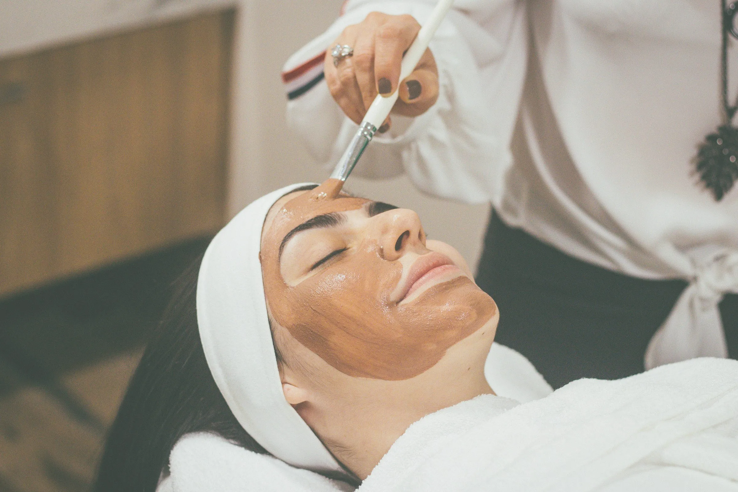 A clay mask being brushed onto a client's face during a facial